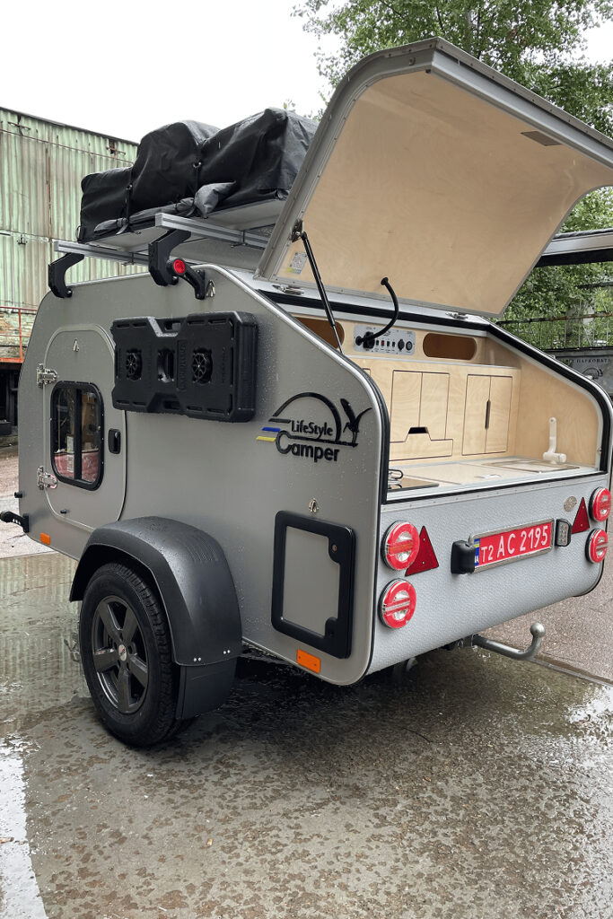 Caravane SIMPLE DROP LifeStyleCamper avec hayon ouvert et cuisine arrière, mini caravane teardrop légère pour escapades nature.